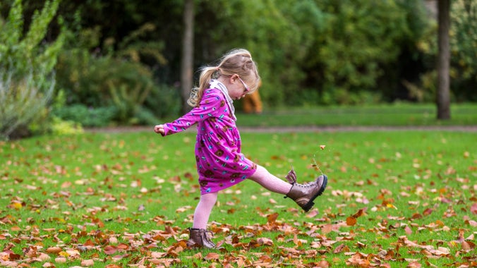 Girl kicking autumn leaves in a garden